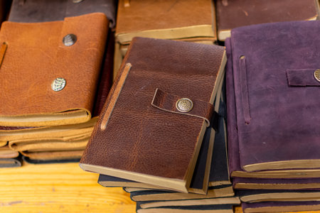 Stack of vintage leather notebooks and journals with button closures on wooden table, warm rustic...