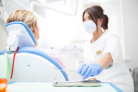 A close-up photo of a dentist's hand taking a sterile instrument from a metal tray. Focus on the doctor's handの写真素材