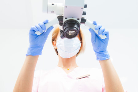 A female dentist is looking into a dental microscope. Bottom view. Focus on the doctor