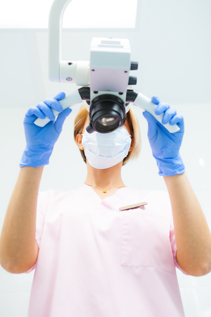 A female dentist is looking into a dental microscope. Bottom view. Focus on the doctorの写真素材