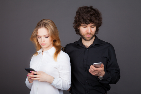 young blond woman and curly-haired brunette man looking in their smartphones. Photos taken by the studioの写真素材