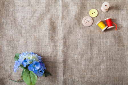 colored threads and wooden buttons and a flower lie on a sackcloth in the corner of the frameの写真素材