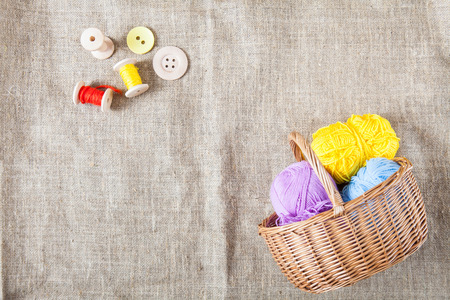 balls of colored threads and wooden buttons and a wicker basket are on sackcloth in the corner of the frameの写真素材