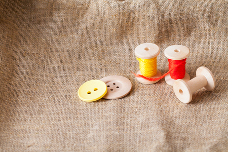 colored threads and wooden buttons lie on sackcloth in the corner of the frameの写真素材