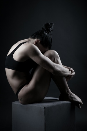 Photo of a young sports woman athletic build in a swimsuit. Theme sports and bodybuilding. Woman on a black background sits curled upの写真素材