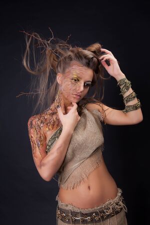 Young beautiful nude woman in the image of a tree. Hairdo with branches. Shooting in a photo studio on a black backgroundの写真素材