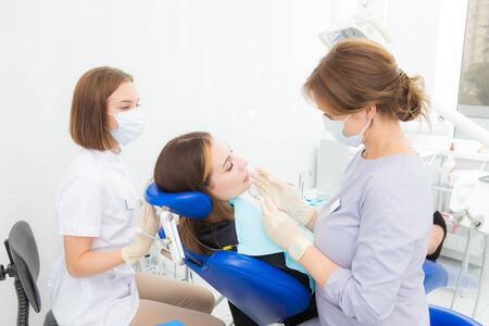 a woman dentist with an assistant treats a tooth to a woman in a modern dental clinicの写真素材