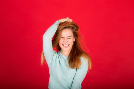 Happy beautiful girl smiling with closed eyes touching her red curly hair on a red backgroundの写真素材