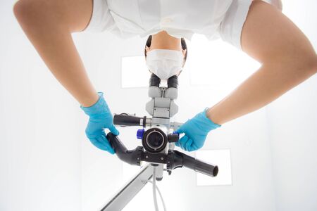 A female dentist is looking into a dental microscope. Bottom view.の写真素材