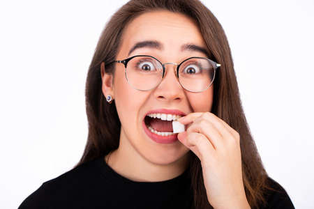 Portrait of a young woman in glasses bites a piece of white sugar. Surprised lookの写真素材