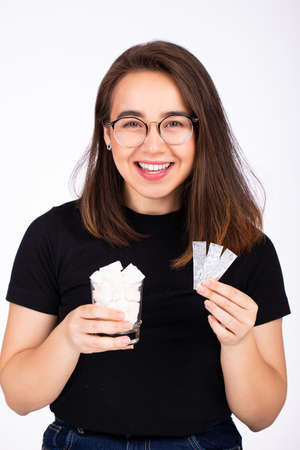 young beautiful woman in glasses with a smile, holds in one hand a glass of white sugar, in the other hand a plate of chewing gumの写真素材