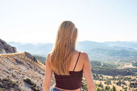 Young beautiful blonde woman looks at the horizon. The traveler stands in the mountainsの写真素材