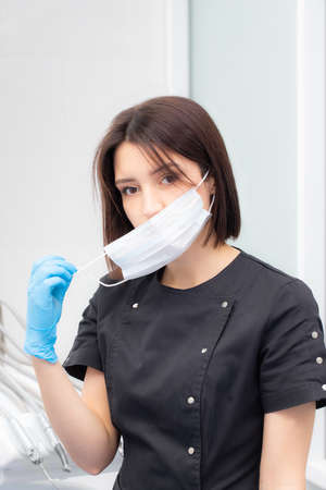 Portrait of a young female doctor in a medical mask is taken off and put on. Medical face mask professional breathing protectionの写真素材