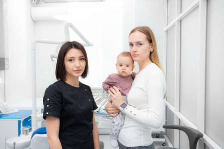 beautiful young woman with a baby in her arms in a dental clinic with a pediatric dentist look at the camera. first visit to the dentist. mother and childの写真素材