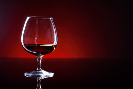 Cognac in a glass on a black table with dark red gradient background