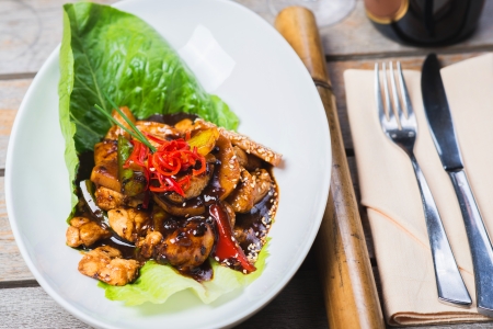 pieces of chicken cooked in black bean sauce on a wooden table in a restaurant with white wine and decorated with an Asian backgroundの写真素材