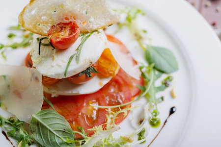 Plate of healthy classic caprese salad with mozzarella cheese, tomatoes and basil on a wooden table...