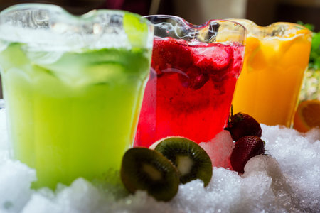 a mix of several bright colored delicious cold lemonade carafes of kiwi and orange and strawberry on...