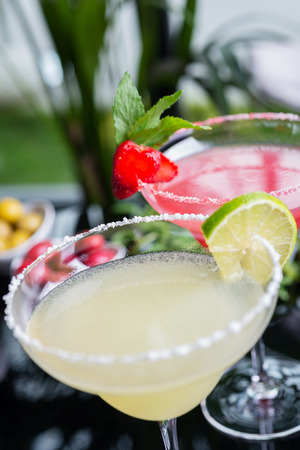 a mix of the two bright refreshing cocktails: lime daiquiri and strawberry daiquiri on a table in a restaurant with creative decoration of salt on the edge of the glass with fresh mint and lime slices and berries. soft focusの写真素材
