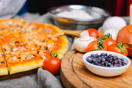 Delicious homemade pizza with cheese and mushrooms on a wooden table with a creative decoration tomato cheese eggs and other ingredientsの写真素材
