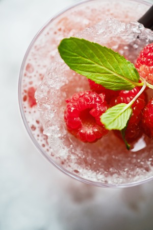 bright beautiful and tasty alcoholic cocktail or lemonade with a cap of frozen ice and fresh raspberries on the bar with a nice bokeh of the disco light. soft focus.の写真素材