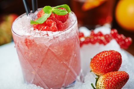 bright beautiful and tasty alcoholic cocktail or lemonade with a cap of frozen ice and fresh raspberries on the bar with a nice bokeh of the disco light. soft focus.の写真素材