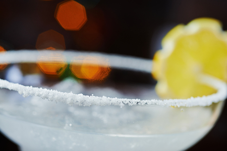 one bright refreshing cocktail daiquiri on a table in a restaurant with creative decoration of orange slices and ice on a wooden table in a bar or restaurant with a beautiful dance disco lights bokeh in the background. soft focus.の写真素材