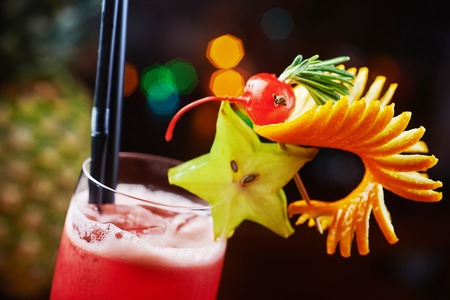 refreshing tasty red alcohol raspberry cocktail or lemonade in a glass with a backdrop of berries and pieces of fruit on a table in a restaurant with backgrounds of bright colorful disco lights. soft focus.の写真素材