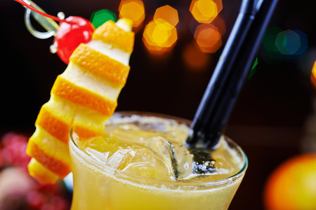 bright tropical alcoholic cocktail or lemonade with slices of orange and beautiful decoration on a table in a restaurant with backgrounds of bright colored lights. soft focus.の写真素材