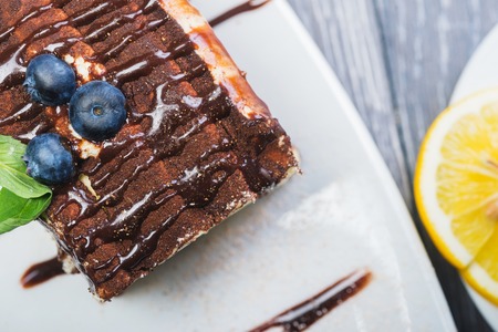 A tiramisu and a cup of tea on the white plate with blueberries and a mint on the woden tableの写真素材