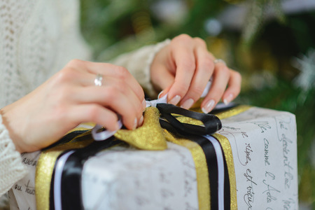 Holiday, celebration concept - hands of a young girl close-up sitting on the floor next to their Christmas tree and opening New Year gifts. Soft focusの写真素材