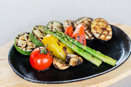 mix of tomatoes, asparagus, zucchini, bell peppers and mushrooms grilled and served on a wooden plate on a table in a restaurantの写真素材