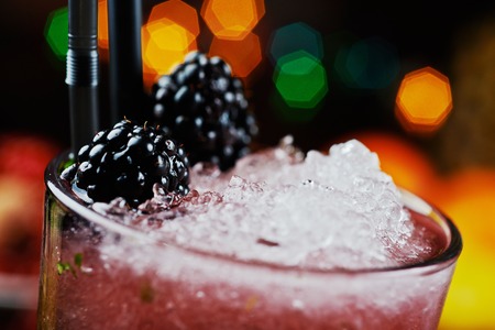 close up of bright beautiful and tasty cocktail or lemonade with a cap of frozen ice and fresh berries on the bar with a nice bokeh of the disco light. soft focus.の写真素材
