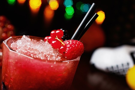 bright beautiful and tasty cocktail or lemonade with a cap of frozen ice and fresh berries on the bar with a nice bokeh of the disco light. soft focus.の写真素材