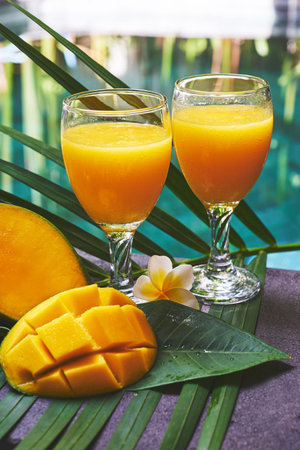 Glasses of fresh tropical smoothie or mango juice and fresh mango on a wooden tabel and tropical background. Soft focus.の写真素材
