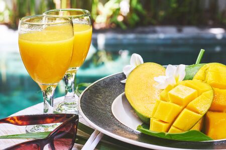 Glasses of fresh tropical smoothie or mango juice and fresh mango on a wooden tabel and tropical background. Soft focus.の写真素材