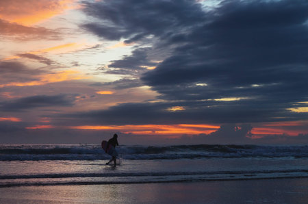 Beautiful tropical sunset with pastel colors. Silhouette of a surfer on the waves, pink clouds and...