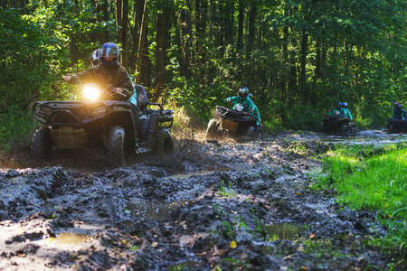 Summer Activities for adults - a trip on quad bikes on the road. Man on ATV in the mud on the road to participate in the race over rough terrain in the forest on a hot summer day.の写真素材