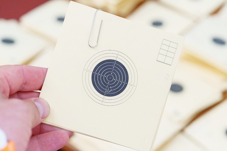 Man holding a paper target at a shooting range with a hole after being hit by small arms fire. shooting competitions in the dash - man estimates the number of hits in a target.の写真素材