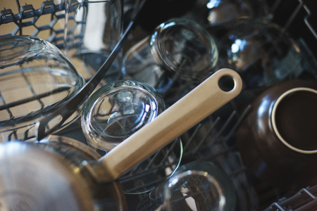 Closeup of clean dishes in the dishwasher loading lattice. Transparent glass cup, steel pan and dishes after washing. Order and cleanliness of the kitchen. Modern household appliances in the home.の写真素材