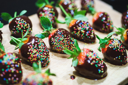 Closeup view of gourmet dessert with strawberries in chocolate decoration on a wooden board. Tasty dessert of berries - a row on a wooden board. Soft focus, color correction and processing.の写真素材