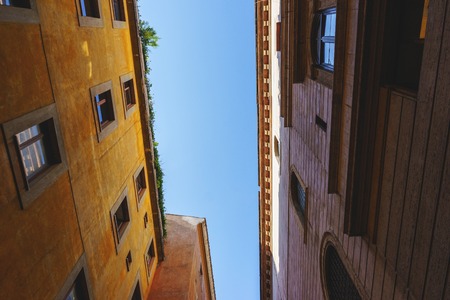 Travel to Rome - the capital of Italy. The narrow streets of the old town, the house and windows with shutters. Blue summer sky above the European beautiful traditional houses in the city. City landscape.の写真素材