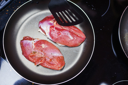 Top view of three large fresh piece of meat in a frying pan. The process of making turkey breast - roasting meat on a grill pan on an induction hob. The process of cooking. Soft focus.の写真素材