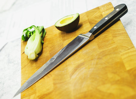 The process of cooking and slicing food from vegetables. Cutting board and knife close-up on the kitchen table. Avocado and greens. Soft focus.の写真素材