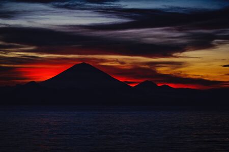 Bright tropical sunset and silhouettes of Agung volcano on the island of Bali in Indonesia. Magic colors during sunset, bright clouds and red sun light. Journey to a tropical island in the ocean.の写真素材