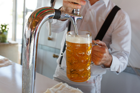 Barman pours a light foamy beer into a large mug during the Oktoberfest party. Festival. Soft focus.の写真素材