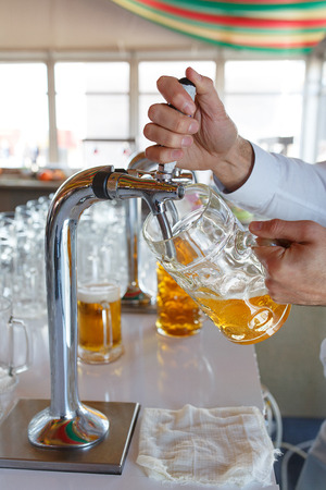 Barman pours a light foamy beer into a large mug during the Oktoberfest party. Festival. Soft focus.の写真素材