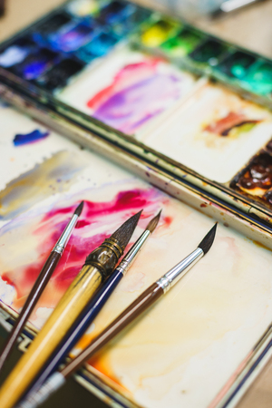 Details of the creative process of the artist, palette with watercolor paints and brushes. School of Art and Drawing Lessons. Soft focus and beautiful bokeh.の写真素材