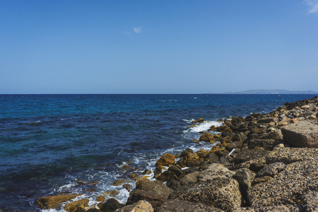 Summer holidays in Greece. Beautiful blue sea and a beach with huge stone blocks. Rest on the beach. Seascape. Dream view of the waves, rocks and deep blue sea. The Mediterranean coast.の写真素材