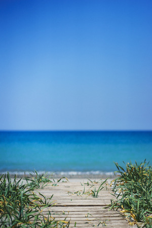 Beautiful seascape wallpaper. Wooden walkway to the beach with green grass and blue sea on the horizon. Soft focus and beautiful bokeh.の写真素材